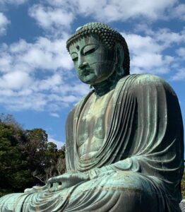 Buddha sitting with clouds, blue sky and trees