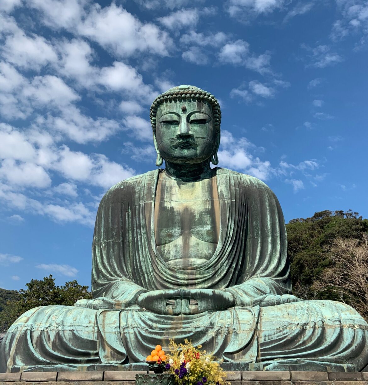 Sitting Buddha with blue sky, clouds, and flowers